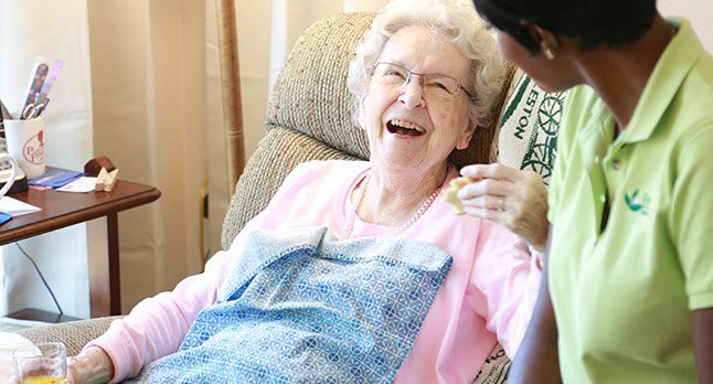 An elderly woman laughing joyfully while sitting indoors.
