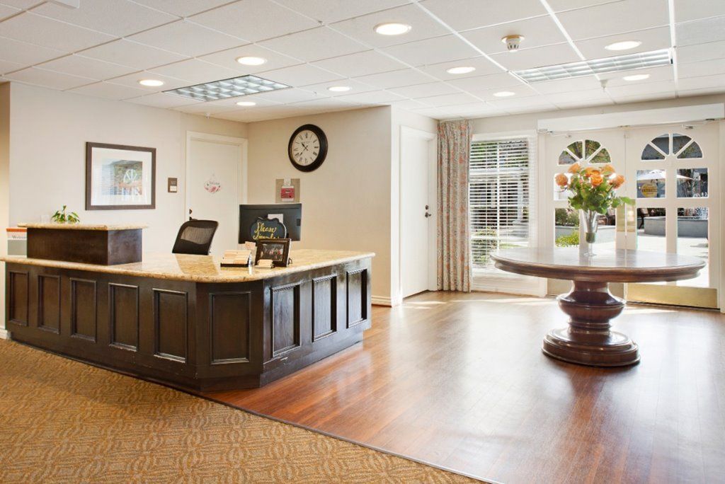 A welcoming office reception area featuring a large desk with a computer, wall clock, and bright natural light from the windows.
