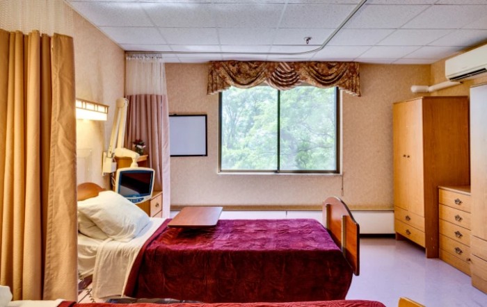 A hospital room featuring a bed, television, and window with curtains.