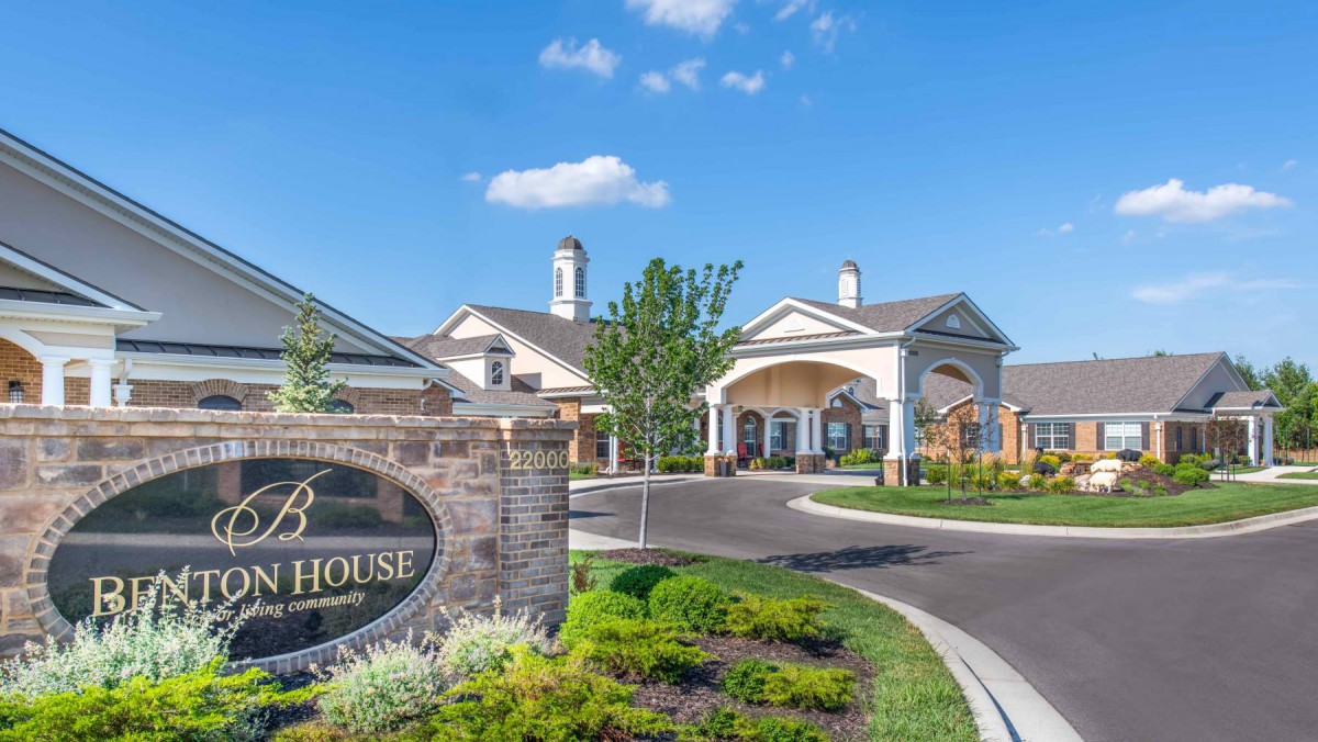 A well-maintained residential entrance with landscaped greenery and clear skies.