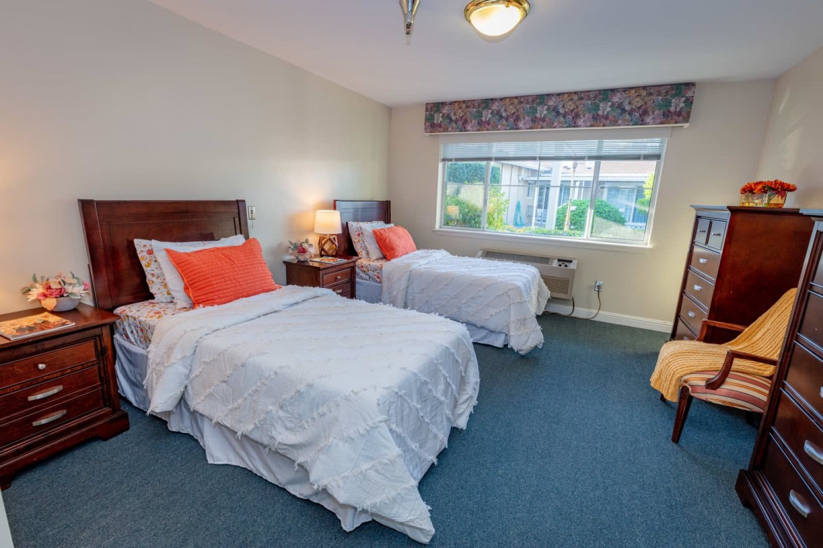A neatly arranged bedroom with two single beds and a large window letting in natural light.