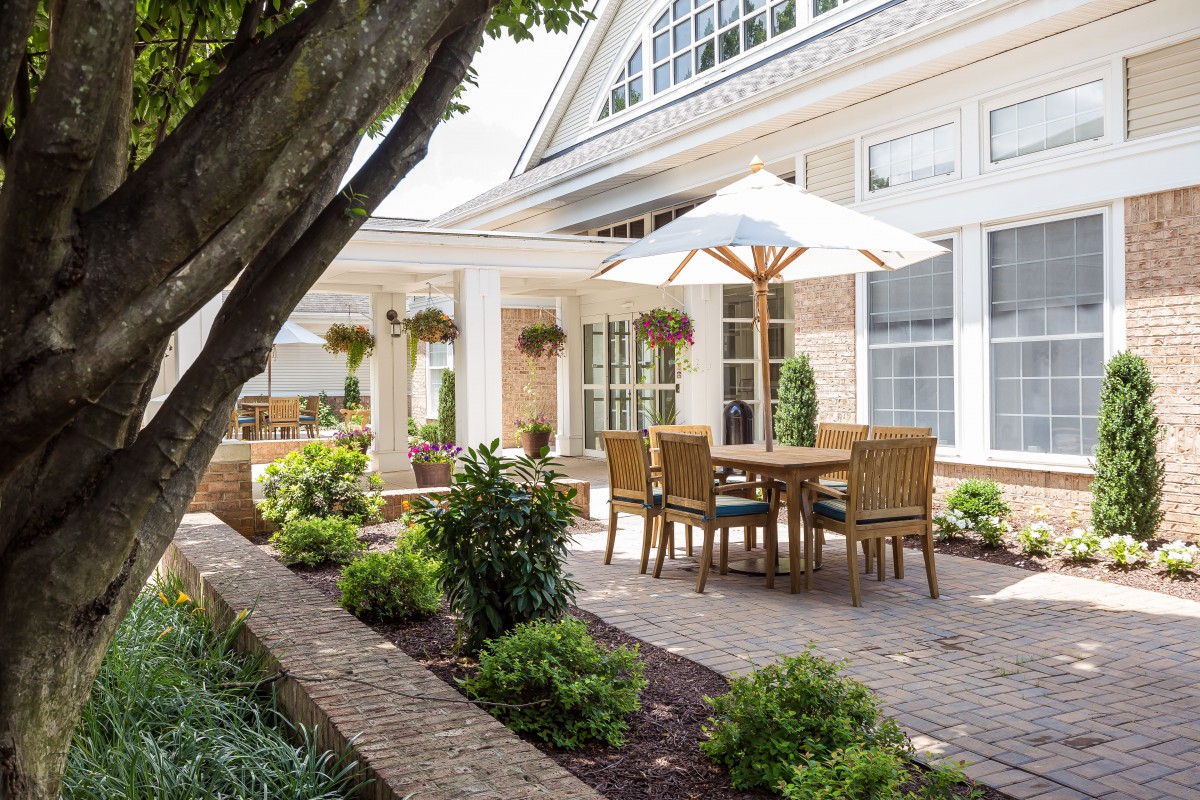 Elegant patio with a dining set and umbrella, surrounded by lush landscaping.
