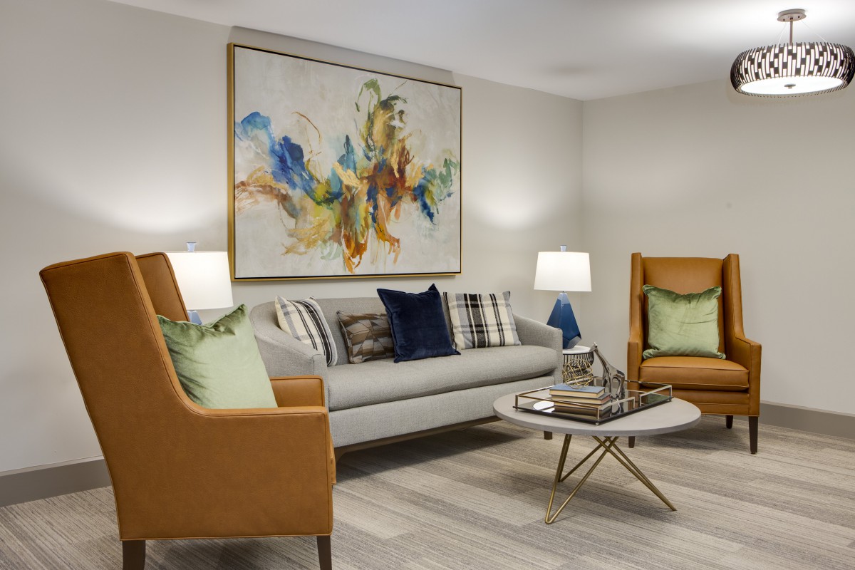 A modern living room featuring a gray sofa, two brown armchairs, a stylish coffee table, and a large abstract painting on the wall.