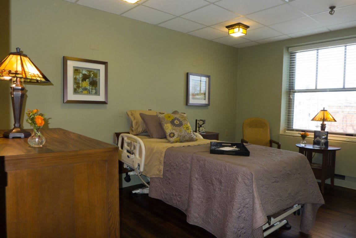 A cozy room with a hospital bed, decorated with green walls and framed artwork.