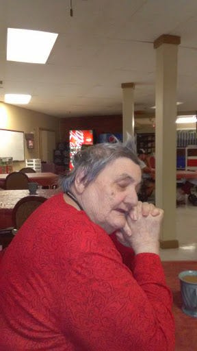 A thoughtful elderly woman in a care facility, dressed in red.