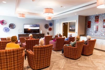 A group of seniors enjoying a communal television viewing in a comfortable lounge setting.