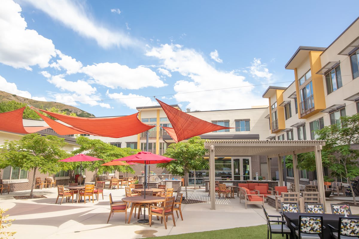 A sunny outdoor patio with tables, chairs, umbrellas, and shade sails.