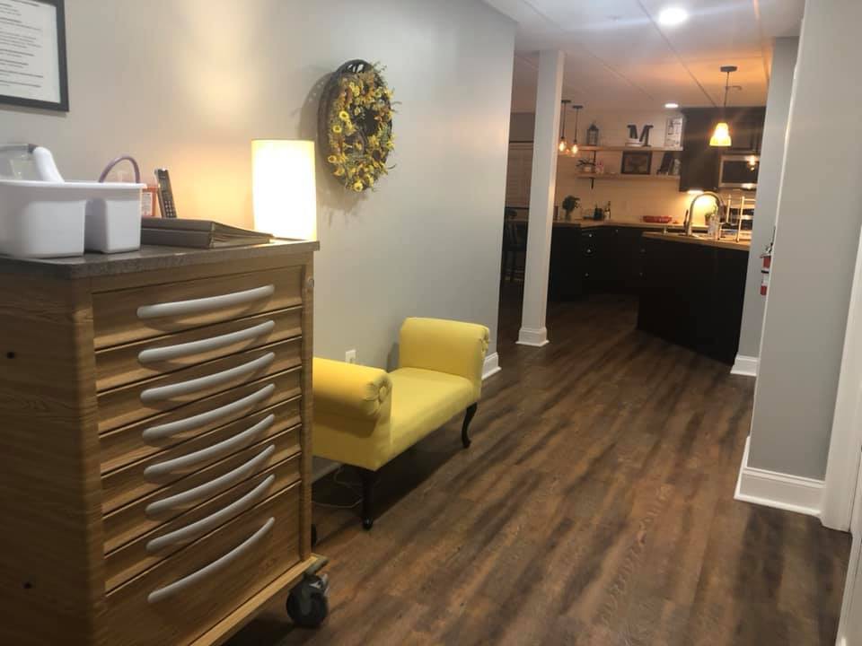 A modern living area with wood flooring, featuring a yellow chair and decorative elements leading into an open kitchen.