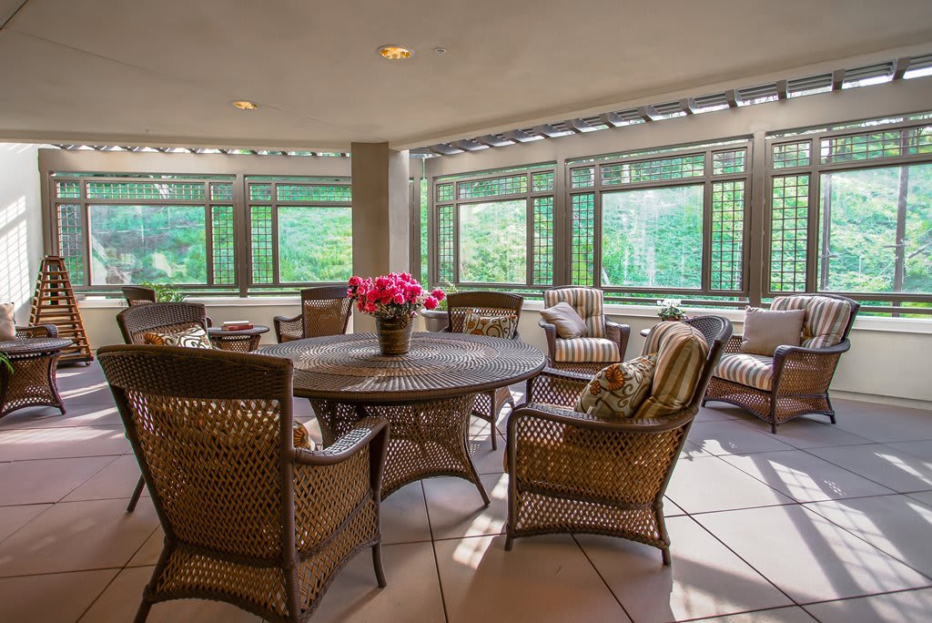 A cozy indoor patio featuring wicker furniture and large windows providing natural light.