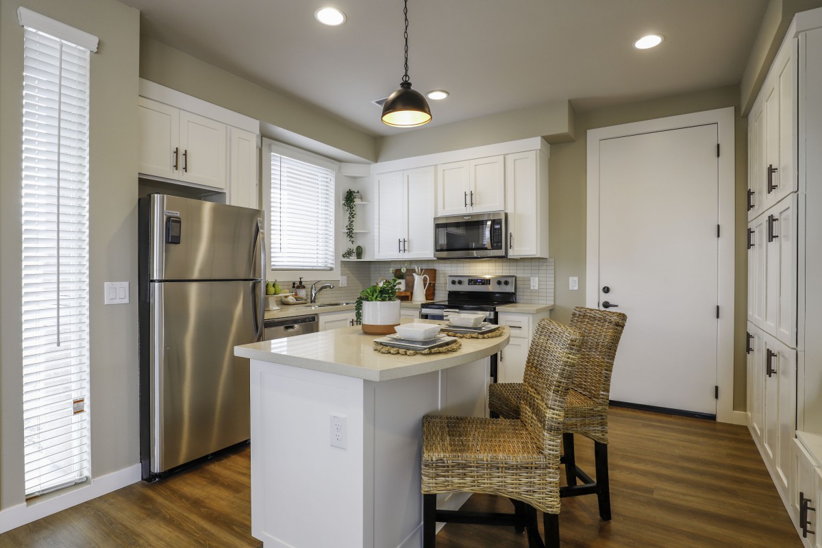 A modern kitchen featuring white cabinets, an island with bar stools, and stainless steel appliances.