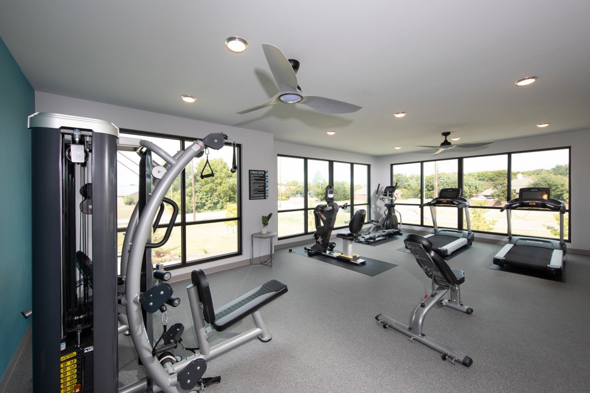 A well-equipped gym with exercise machines and large windows providing natural light.