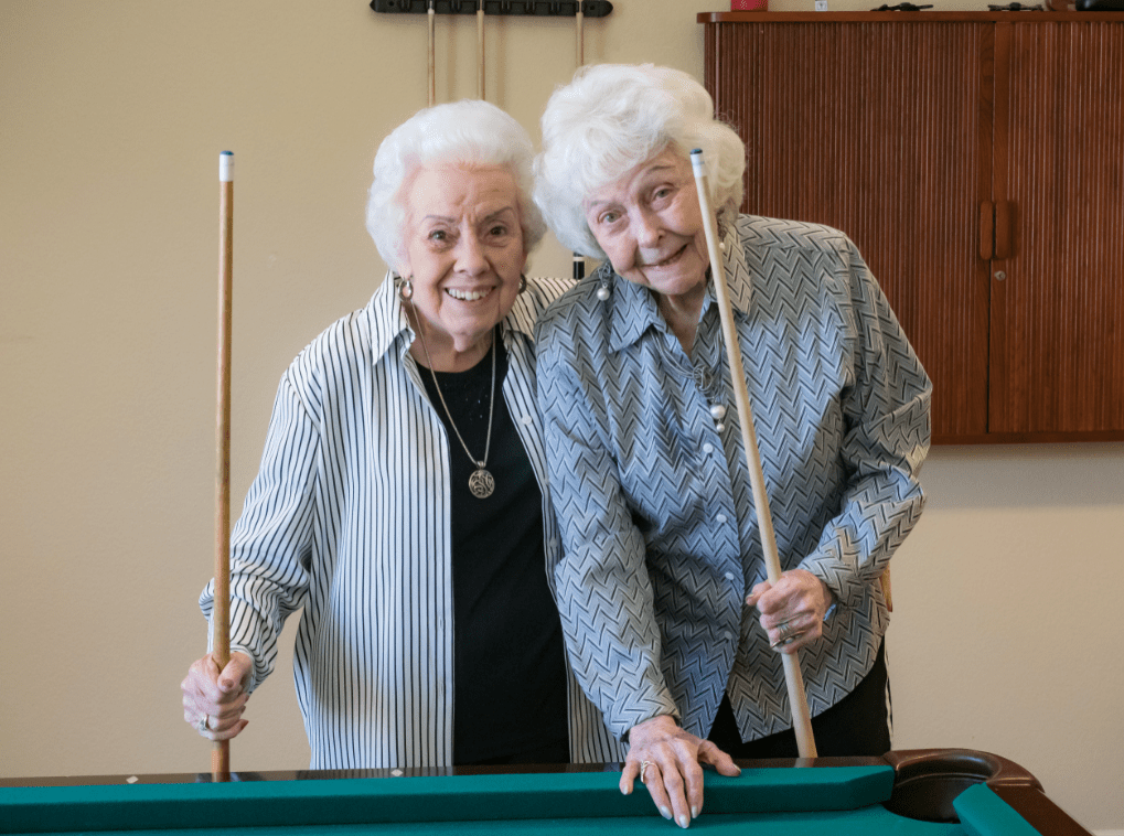 Two elderly women enjoying a game of billiards together.