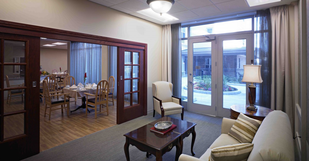 A cozy living room with a view into the dining area, featuring traditional furniture and glass doors leading outside.