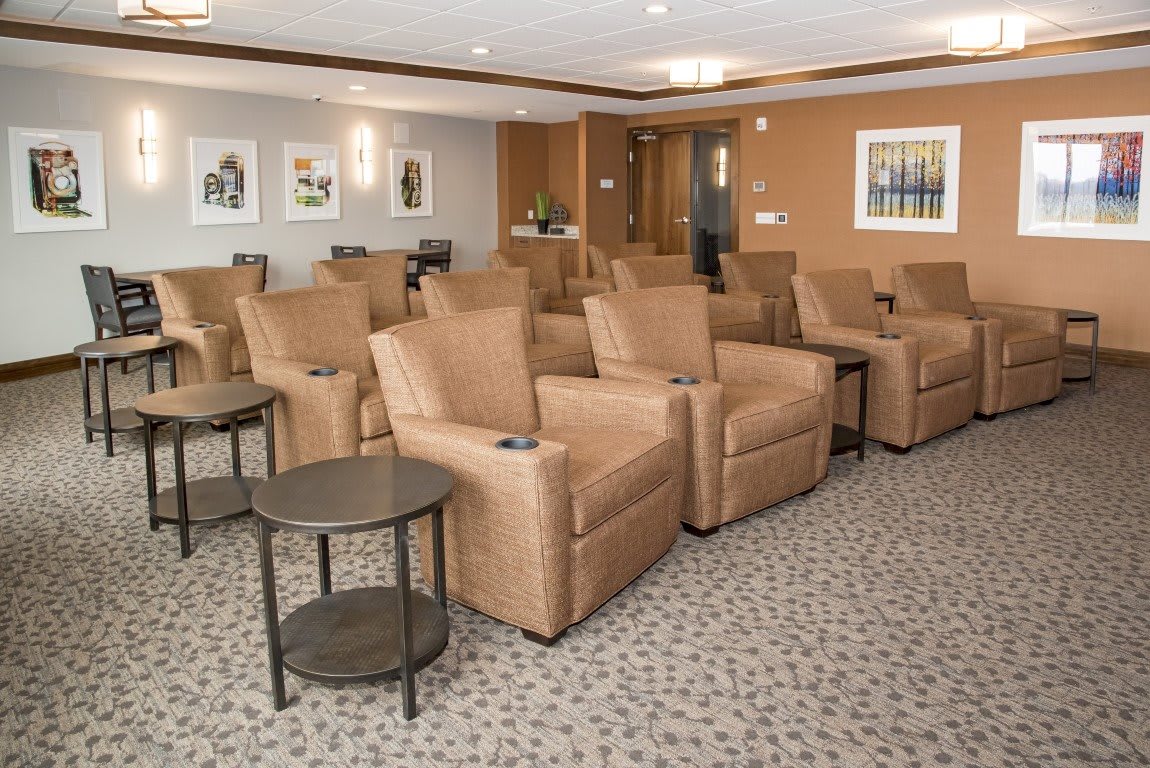 A cozy theater room with rows of beige recliners and side tables, featuring a warm interior design.