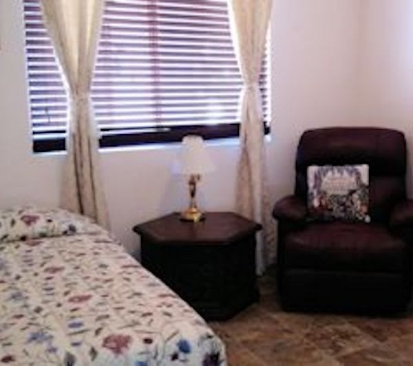 Cozy bedroom with a bed, armchair, and a lamp on a side table near the window.