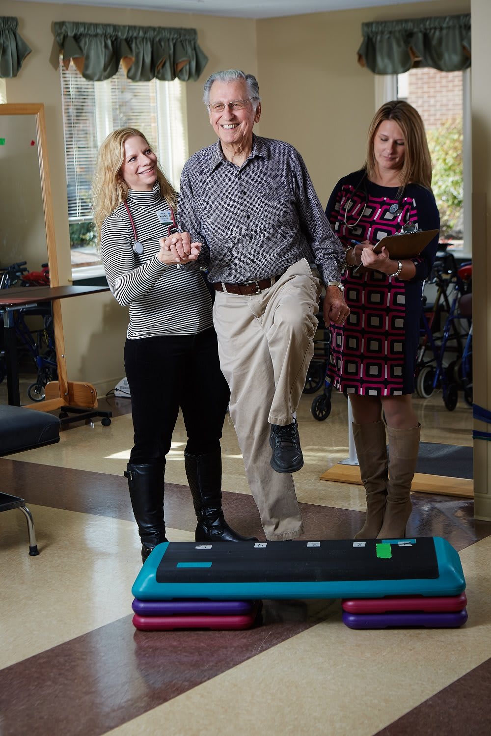 An elderly man participates in a balance exercise with the assistance of healthcare professionals.
