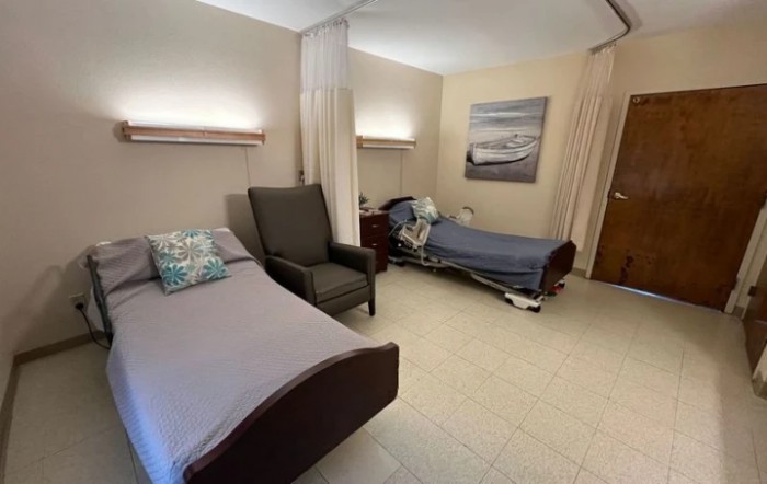 A hospital room with two beds, a chair, and privacy curtains.