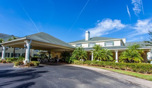 A hotel entrance with a covered driveway and palm trees under a clear blue sky.