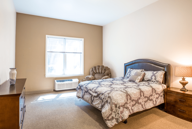 A cozy bedroom with a large bed, armchair, and ample natural light from the window.