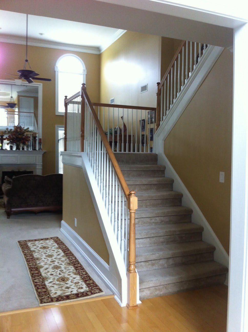 A well-lit home interior featuring a carpeted staircase with wooden railings leading to the upper floor.
