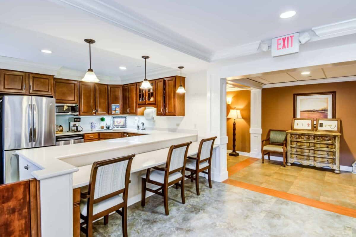 A modern kitchen with wooden cabinets, a long countertop with bar stools, and pendant lighting.