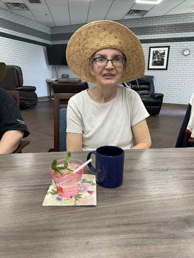 A woman enjoying a drink at a social event, wearing a stylish straw hat.