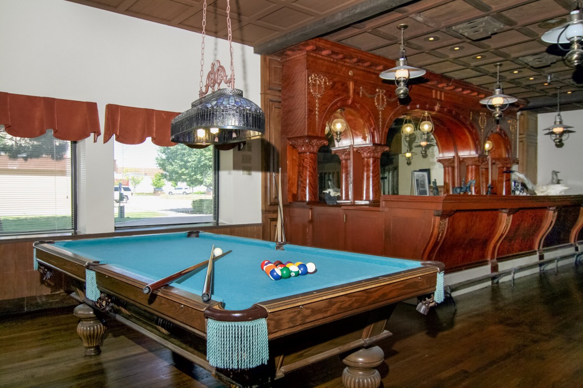 A stylish recreation room featuring a pool table and a classic bar setup with wooden paneling.