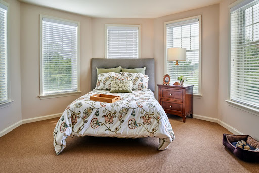 A cozy bedroom featuring a neatly made bed with patterned bedding, natural light streaming in through multiple windows, and stylish furniture.