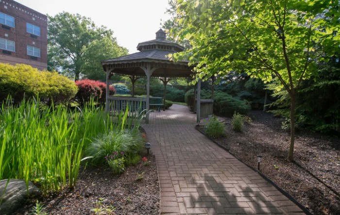 A tranquil garden scene with a pathway leading to a gazebo surrounded by lush greenery.