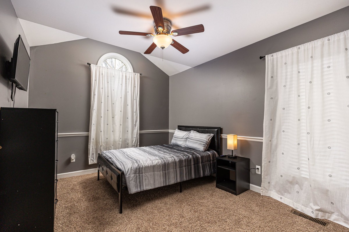 A modern bedroom featuring a neatly made bed, soft carpet flooring, and stylish decor with a ceiling fan above.