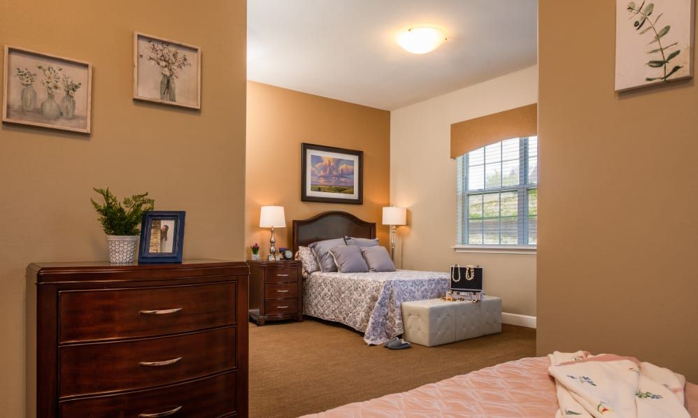 A well-decorated bedroom with warm tones, featuring a bed, nightstands with lamps, and a large window.