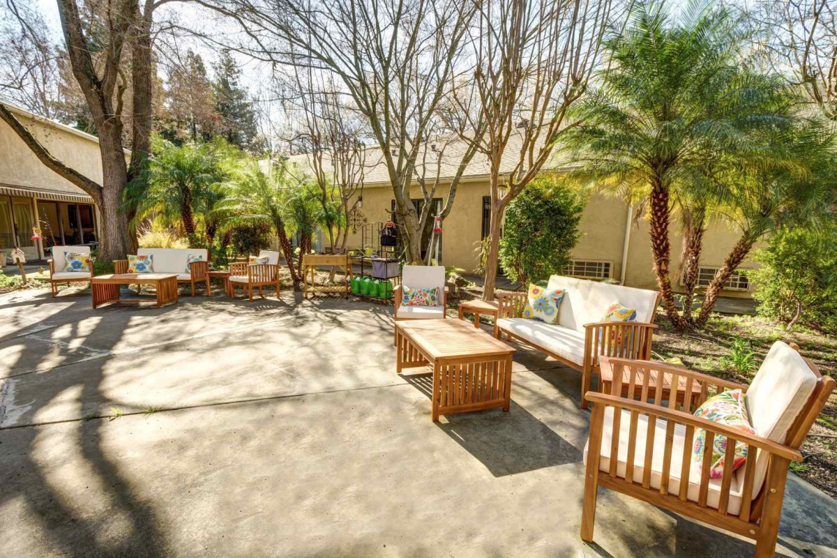 A sunny patio area with comfortable wooden furniture surrounded by lush greenery.