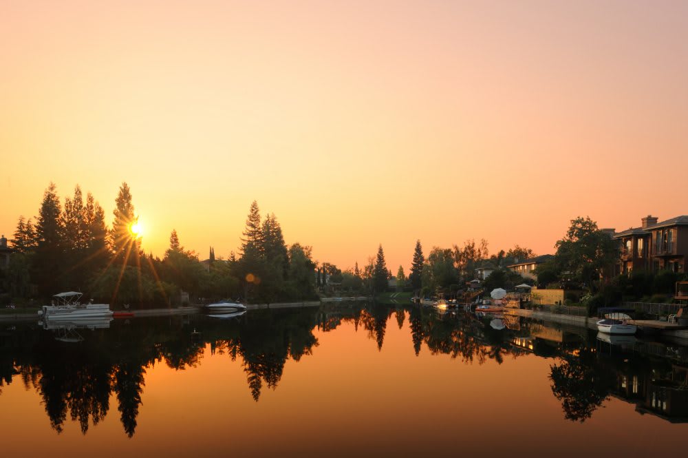 A tranquil sunset over a peaceful river lined with trees and houses.