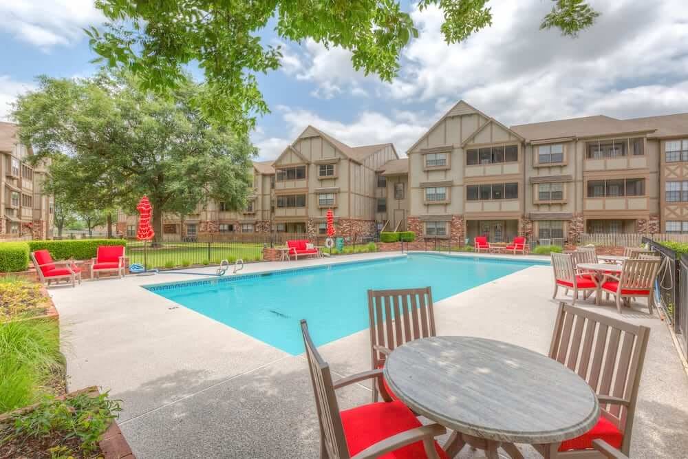 A view of an apartment complex with a swimming pool surrounded by outdoor furniture and trees.