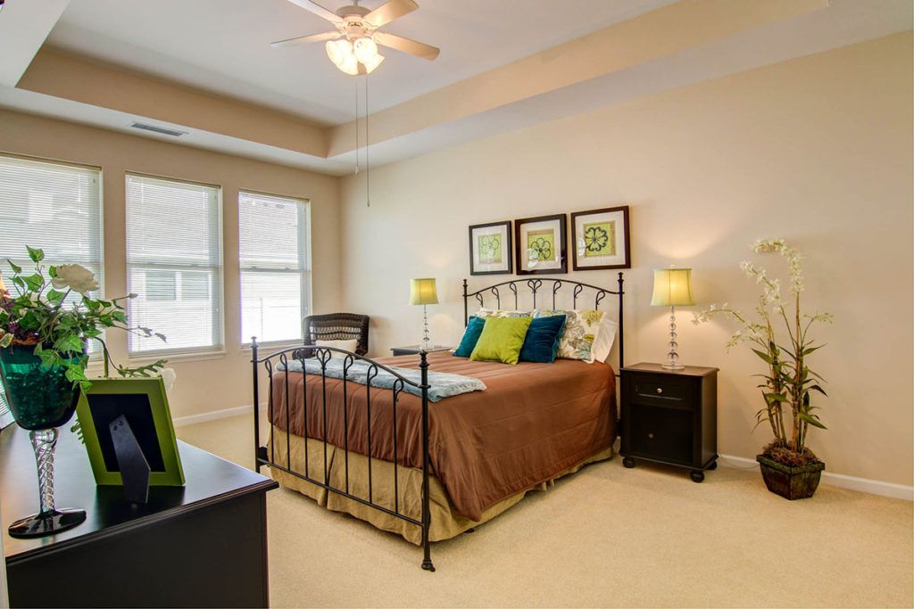 A modern bedroom with a metal-framed bed, decorative pillows, nightstands, and lamps next to large windows.