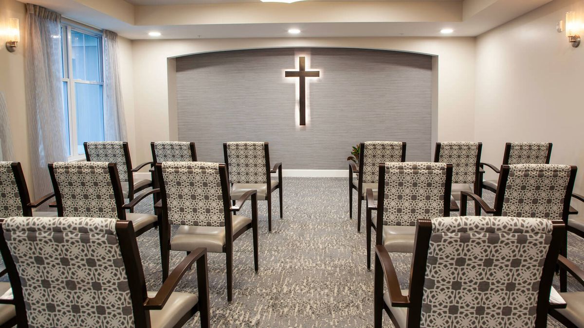 A small chapel interior with rows of chairs facing a wall adorned with a cross.