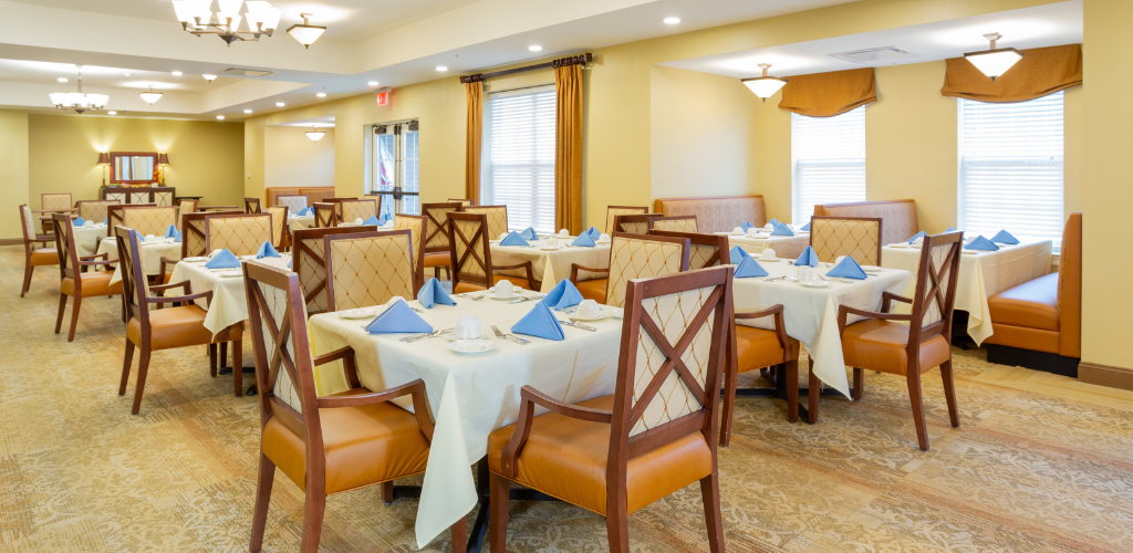 An elegantly set dining room with tables and chairs arranged neatly, featuring blue napkins and warm lighting.