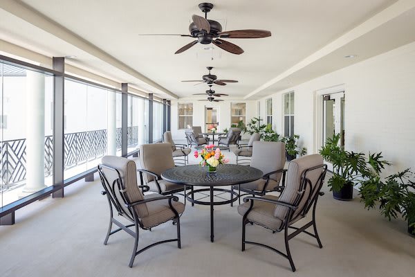 A spacious covered patio featuring a dining set and ceiling fans, with plants enhancing the relaxing atmosphere.