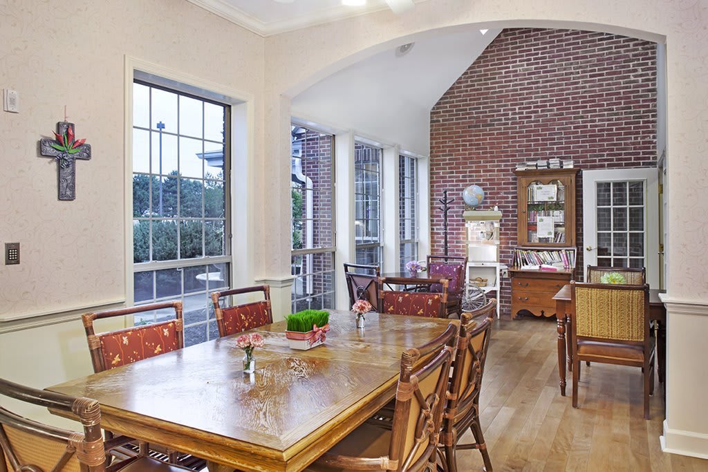A cozy dining area with wooden furniture, large windows, and a brick accent wall.