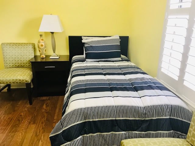 A cozy bedroom with a single bed and striped bedding, accompanied by a nightstand, lamp, and chair.