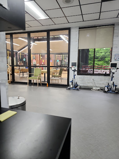 A spacious indoor area featuring modern furniture and exercise equipment, with large windows allowing natural light.