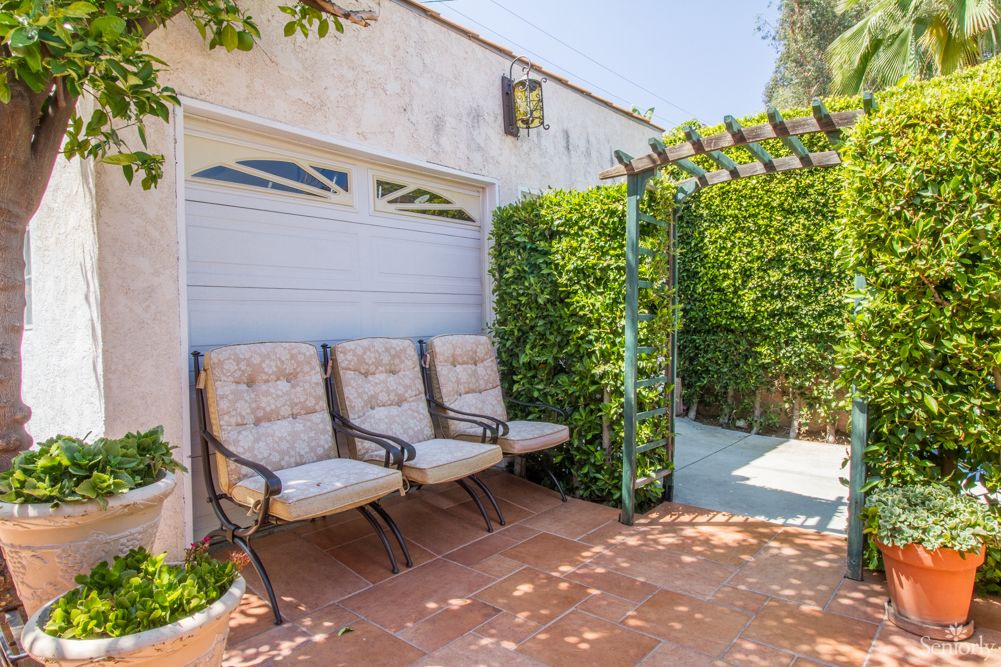 A cozy outdoor patio area with cushioned chairs and a pergola, surrounded by greenery.