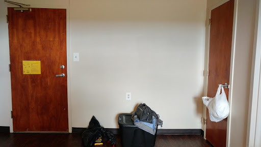 A view of a simple room with a wall, door, and a trash can filled with clothes.