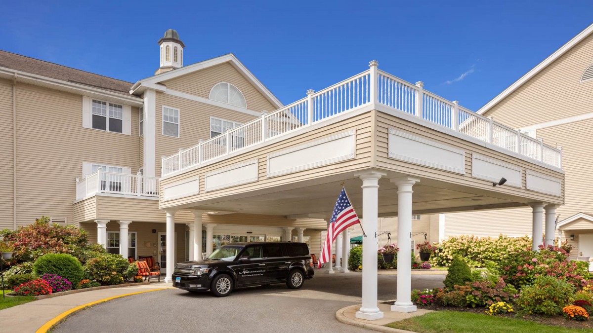 A building entrance with a covered driveway, featuring columns and an American flag.