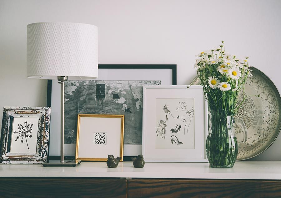 A stylish interior setup featuring a lamp, art frames, and a vase of flowers on a tabletop.