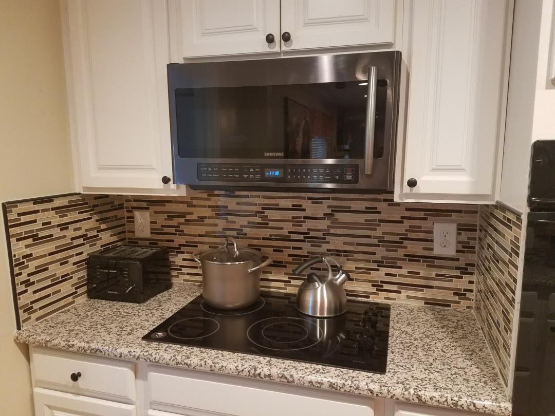 A modern kitchen with a microwave above a stovetop, featuring a pot and kettle on the burners and a decorative backsplash.