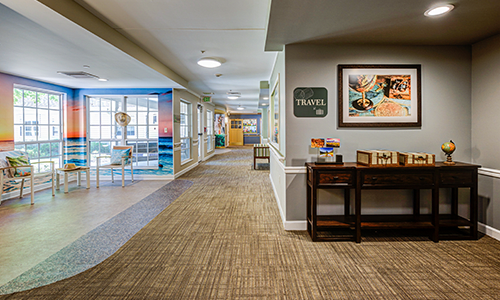 A modern office hallway with carpet flooring, artwork on the walls, and office furniture.