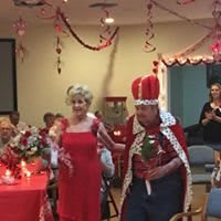 An elderly couple dressed as king and queen celebrate at a festive party.