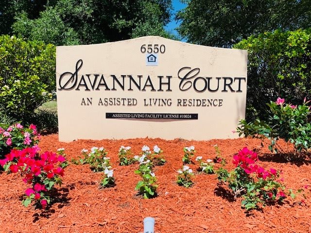 The entrance sign for Savannah Court, an assisted living residence, surrounded by vibrant flowers.