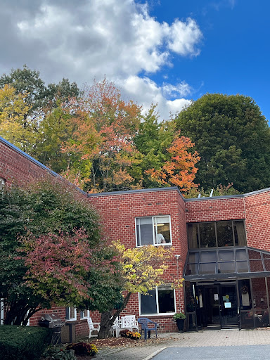A peaceful autumn scene featuring a brick building surrounded by colorful trees under a bright blue sky.